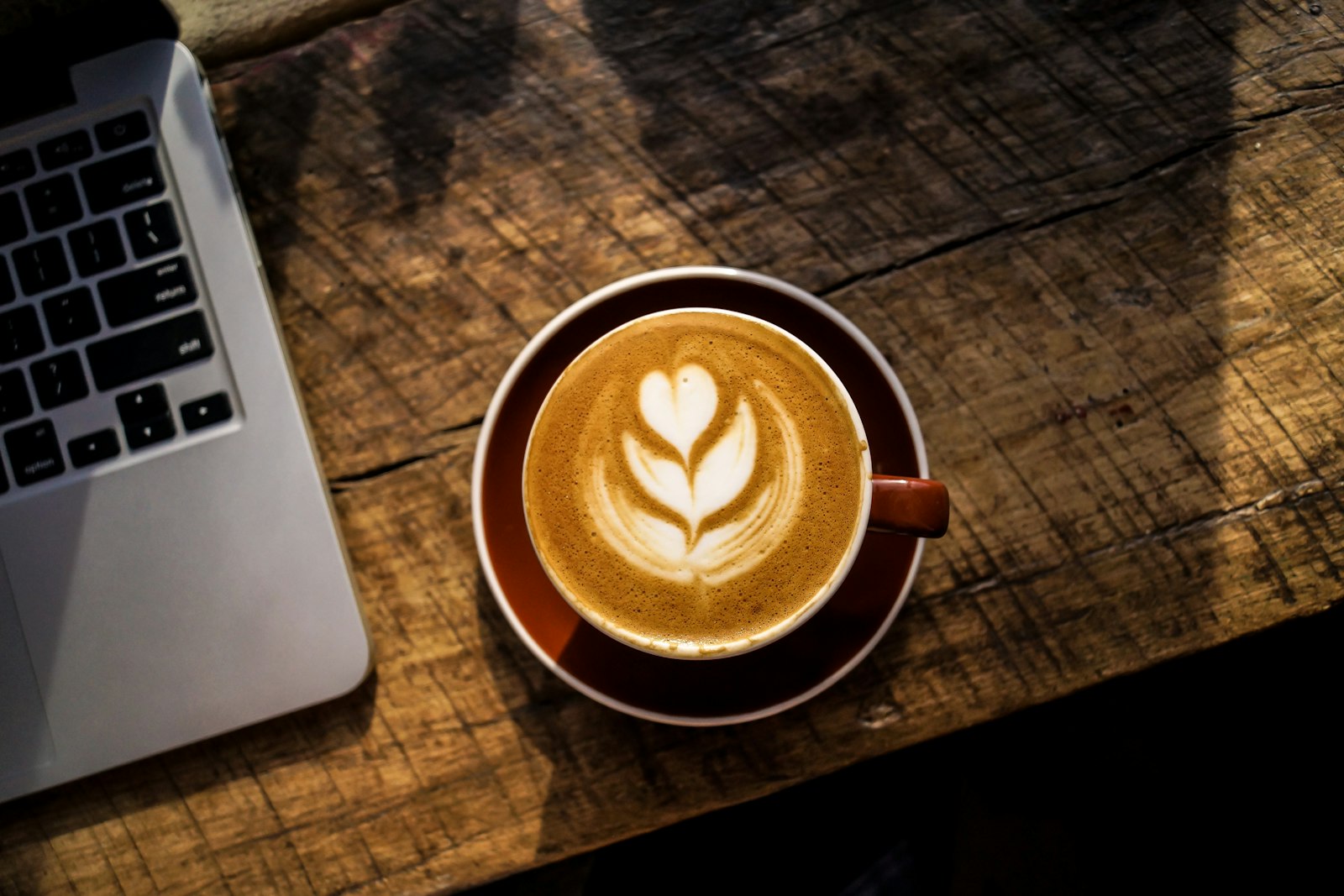 Coffee cup next to a laptop on a wooden table